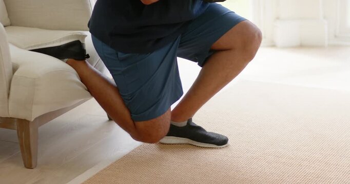 African American man placing left foot on chair, training split squats with weight at home