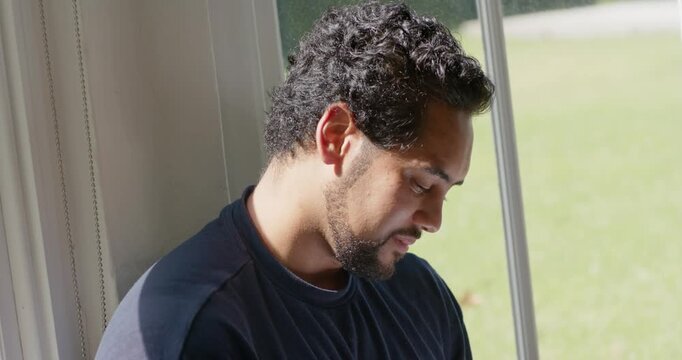 African American man adjusting notebook and reflecting while writing by window with rose-gold pen