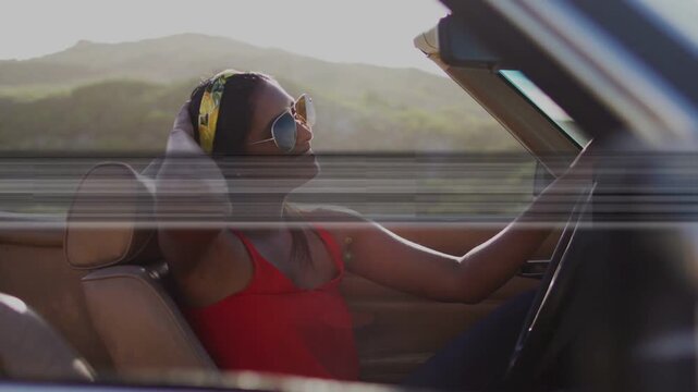 Woman driving droptop past hills wind lifting hair fixing band for comfort, scanline crossing auto