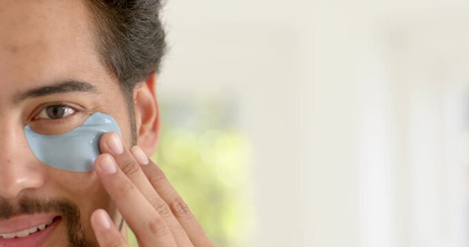Mid adult African descent man bringing, applying and smoothing under-eye patch at sink for skincare