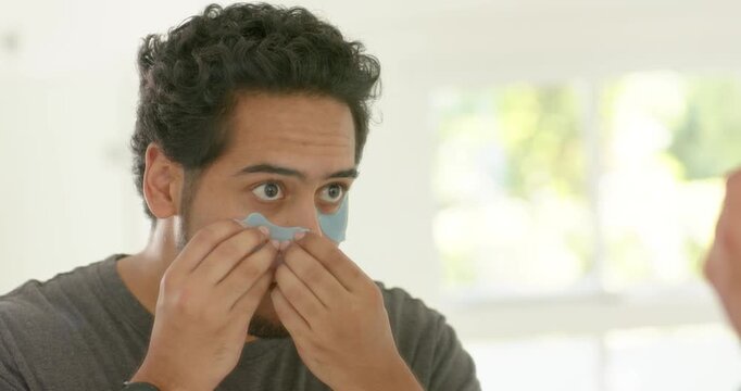 African American man applying 2nd blue undereye patch at mirror, smoothing to reduce swelling