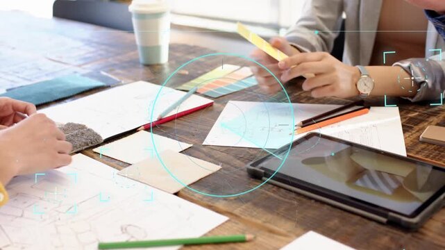 Design team tapping tablet and passing yellow swatch on wooden table, HUD showing color matches