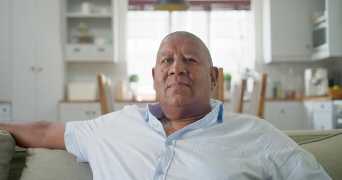Mature African American man sitting in living room on sofa, glancing up left then smiling