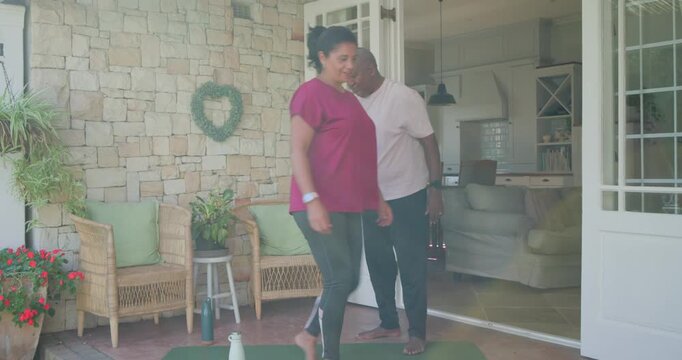 African couple placing water bottles on green mats woman in magenta preparing for workout on porch