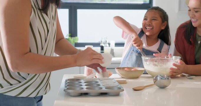 Diverse women, girl cracking eggs pouring milk stirring batter at counter preparing tin for baking