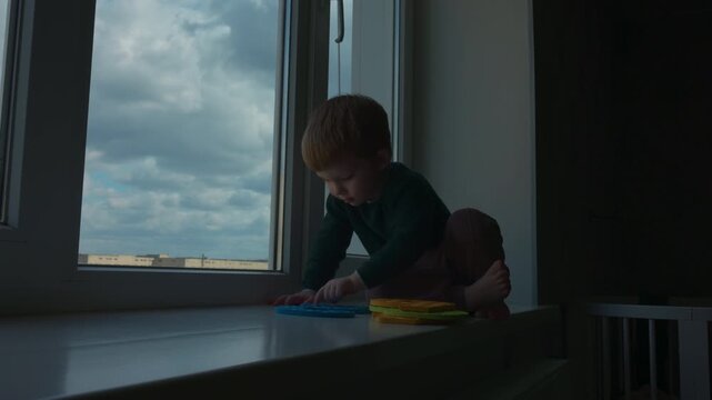 Little boy playing with colorful numbers on the windowsill at home, slow motion
