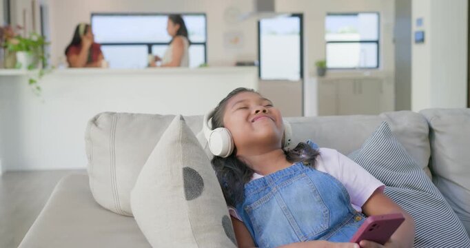 Diverse family, youth girl in overalls tapping pink phone pinging, listening on headset on sofa