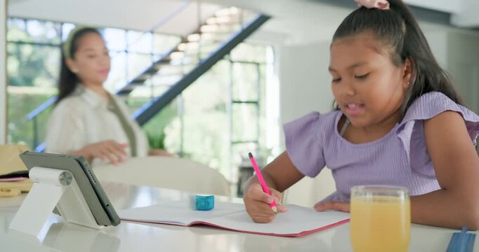 Mother and daughter sitting at home, girl checking tablet as mother guiding pencil to help writing