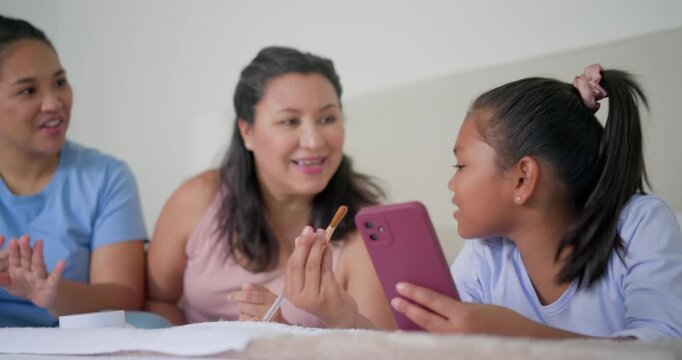 Family guiding girl being prompted by pink smartphone, practicing makeup with brush on bed