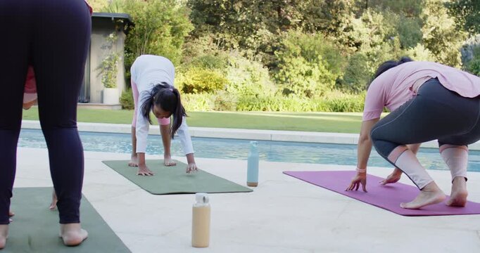 Diverse female yogis moving from standing fold, placing hands on mats to deepen pose at poolside