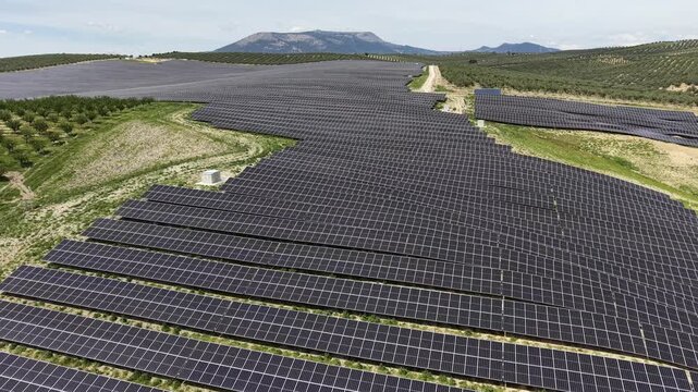 A tracking drone shot moving across the geometric patterns of the Pinos Puente solar array with rolling hills and olive trees in the background.