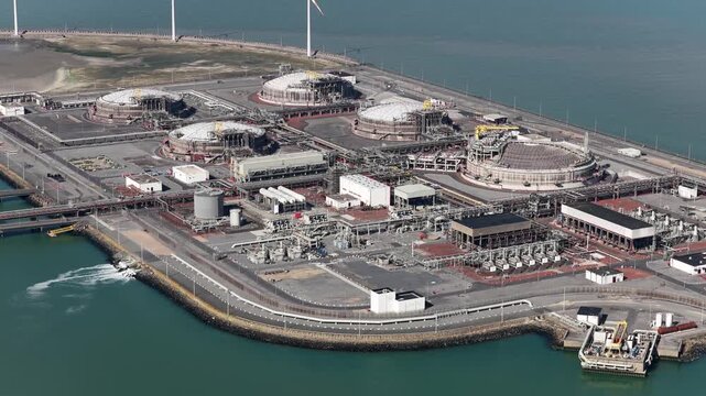High angle view showing a large liquefied natural gas terminal located on a coastal port, complete with storage tanks, processing facilities, and a maritime jetty for tankers