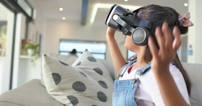African American child wearing VR headset, denim, reaching, smiling at VR scene on sofa, copy space