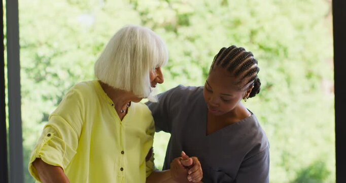 African American nurse gray scrubs steadying senior shifting weight by glass door, ensuring balance