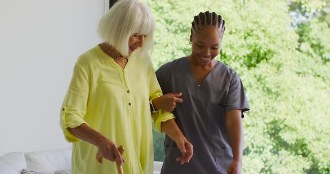 Senior with African American nurse guiding senior using cane near window to assist walking