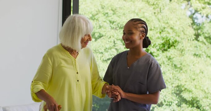 African American caregiver in gray scrubs guiding senior needing support while holding wooden cane