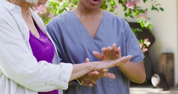 Female caregiver noticing senior's watch, inspecting and guiding hands on porch offering care