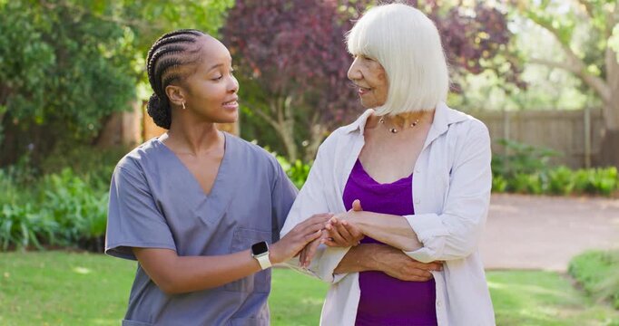 African American caregiver guiding and checking senior wrist for mobility after smiling in garden