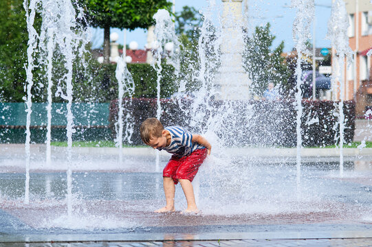 Child playing with water fountain in city square on summer day. Summer lifestyle, joy, freedom and refreshing activity in urban environment.