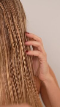Young woman detangling wet blonde hair with fine comb. Close up of tangled strands, difficult brushing and damaged hair care concept