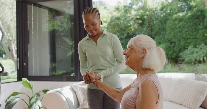 Adult African American caregiver gently taking Senior woman's hand, guiding arm exercise on sofa