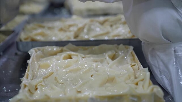 Close-up of gloved hands folding and placing oiled phyllo dough into a tray during borek preparation. Layered dough texture and preparation details are highlighted in a kitchen setting.