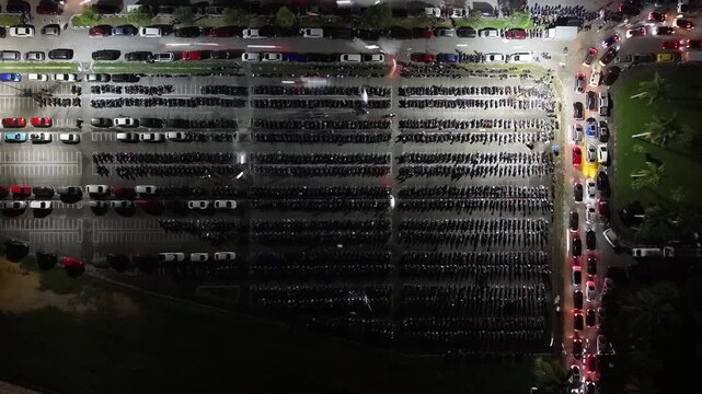 Aerial night view of parked motorcycles and car light trails in a large parking lot at Batu Kawan Stadium