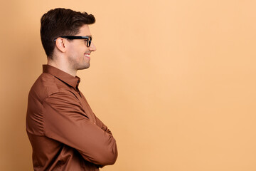 Young man in brown shirt smiling in profile with arms crossed and glasses against neutral background, confident casual portrait with copy space © deagreez