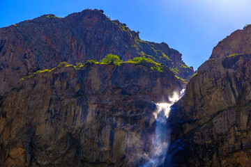 Fototapeta premium Waterfall cascading down rocky mountainside under clear sky
