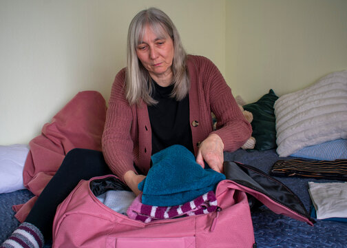 Senior woman placing folded clothes into suitcase preparing for travel
