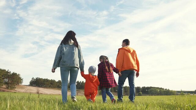 Walking together across green field family parent mother father holding child daughter son hand and walk through meadow under blue sky and soft cloud with open horizon showing peaceful family bonding