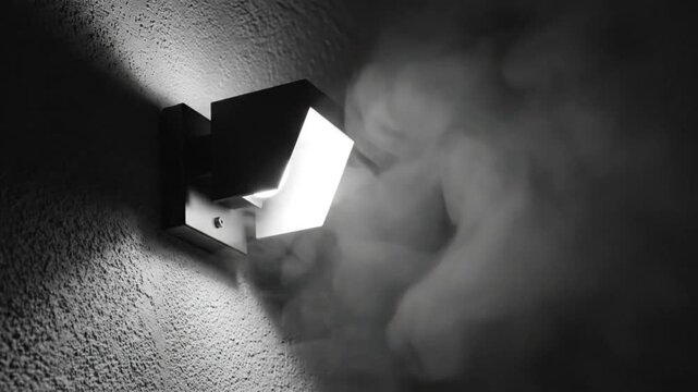 Bright modern geometric wall lamp illuminates smoke against textured dark background creating a dramatic moody atmosphere