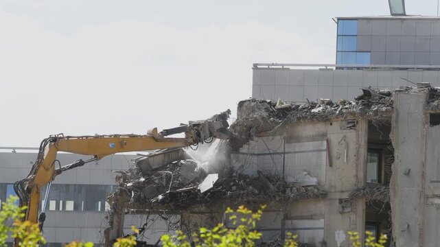 Demolition of reinforced concrete structure, gutting and renovation, hydraulic hammer dismantles building, caterpillar excavator machine at construction site