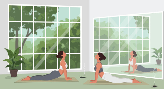 A woman practices the cobra pose in yoga reflected in a large window with lush greenery