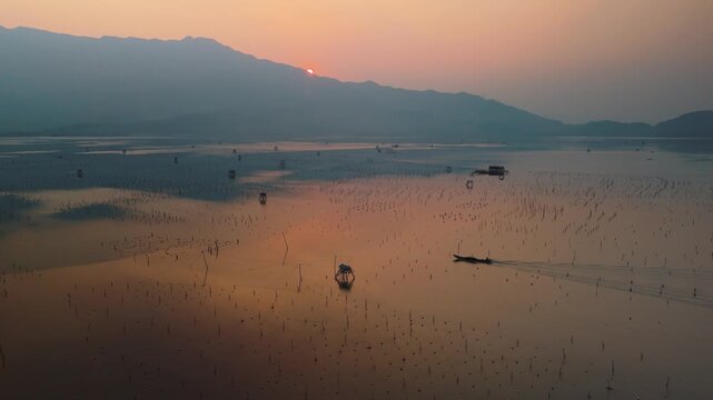 Fishermen's shacks dotting the water's surface amidst countless fishing poles, capturing reflections of the golden hour sky as a longboat navigates the serene, expansive lake during sunset