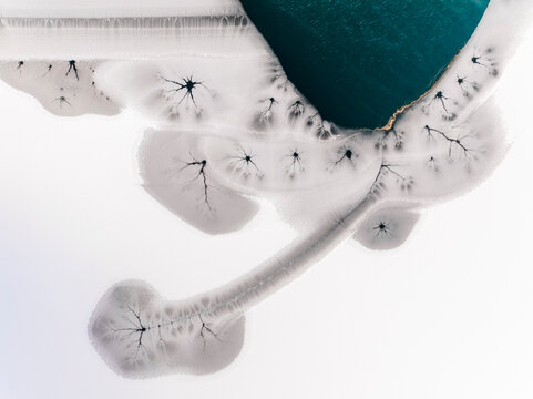 Landscape, aerial view of frozen lake with cracks and turquoise water, abstract nature pattern, destination concept. Fusine lakes, Tarvisio, Friuli, Italy.