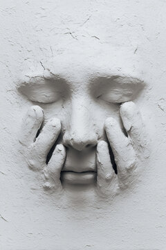  a white clay face being gently pressed by two fingers