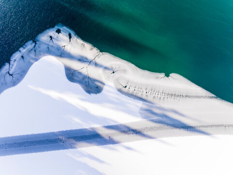 Landscape, tourism: Aerial view of frozen lake meeting open water, creating a unique pattern, suggesting the transition of seasons. Fusine lakes, Tarvisio, Friuli, Italy.