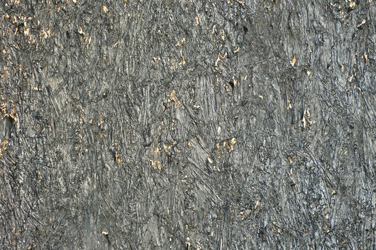 Rough black painted wood chipboard wall texture with layered grain, scratches, and distressed surface background texture. Industrial design, grunge aesthetics. Close-up photo of pressed wood chips.