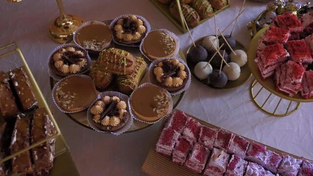 Close-up of elegant dessert table at banquet. Sponge cakes, shortbread cookies, baked goods, and sliced cakes are on the table. Dessert bar with a variety of creamy pastries for celebration.