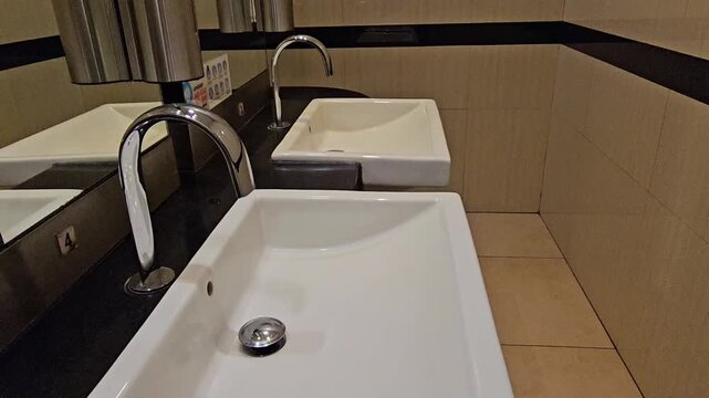 textured surface. ,Modern bathroom with sleek sinks and chrome faucets. Clean white basins reflect light off polished surfaces. Black countertop contrasts with warm beige walls