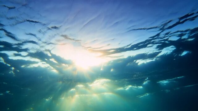 Slow rising tracking shot of sun rays filtering through ocean surface with underwater light beams in open sea at sunrise