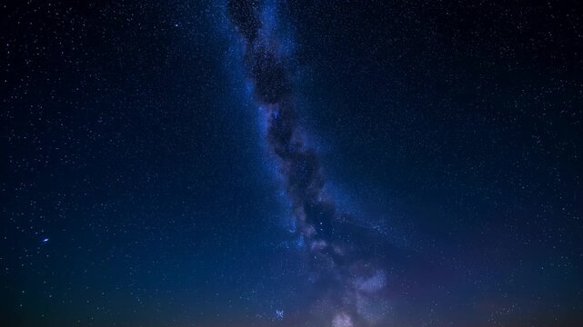 Time lapse vertical pan of milky way rising over distant horizon in remote night sky landscape with star field and celestial band