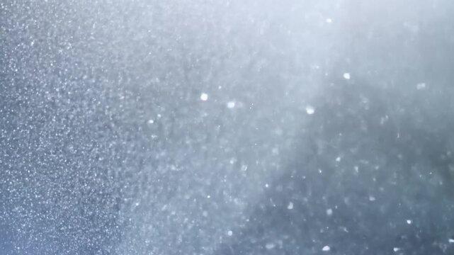 Slow motion closeup of airborne snow particles drifting through misty cold outdoor atmosphere with soft bokeh and shimmering sparkle