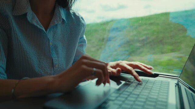 Businesswoman commuting by train, focused on typing on her laptop as countryside scenery passes the window, illustrating remote work, travel and the digital nomad lifestyle