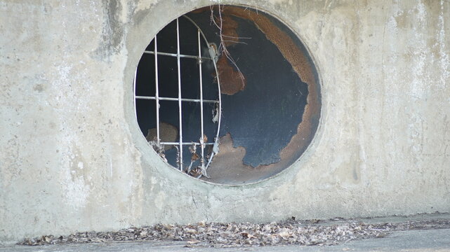 Circular drainage outlet or ventilation hole in a concrete wall with a metal grate