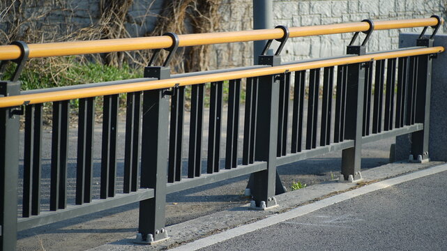 Modern outdoor safety railing with a yellow handrail and black metal pickets on a concrete sidewalk