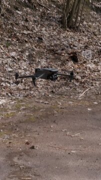 Tactical reconnaissance drone hovering against pine forest background.