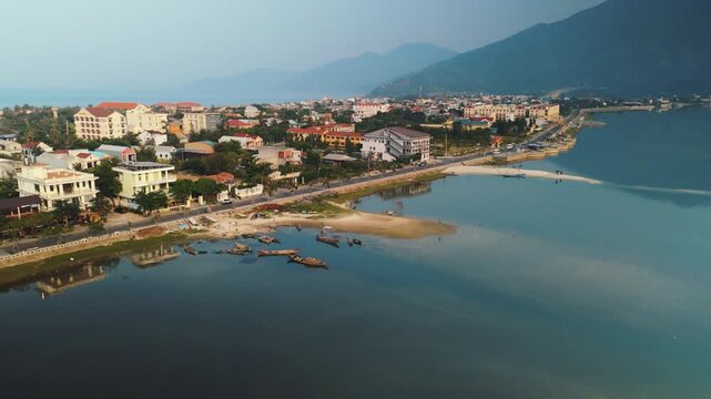 Lang co bay, hue, vietnam, with traditional fishing boats in reflective water near the coastal town, surrounded by mountains under a clear blue morning sky, showcasing tranquil beauty