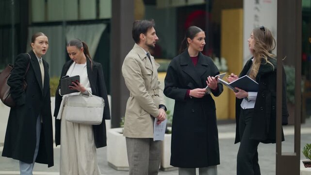 A diverse group of business professionals engages in an outdoor discussion within an urban setting. Colleagues gather to collaborate and exchange ideas on a city street.